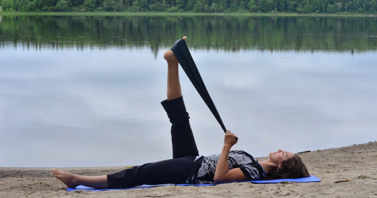 Femme faisant des étirements avec une bande élastique sur le bord d'un lac