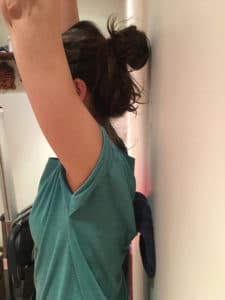 femme se tenant contre un mur les bras relevés avec des balles dans le dos pour faire un massage