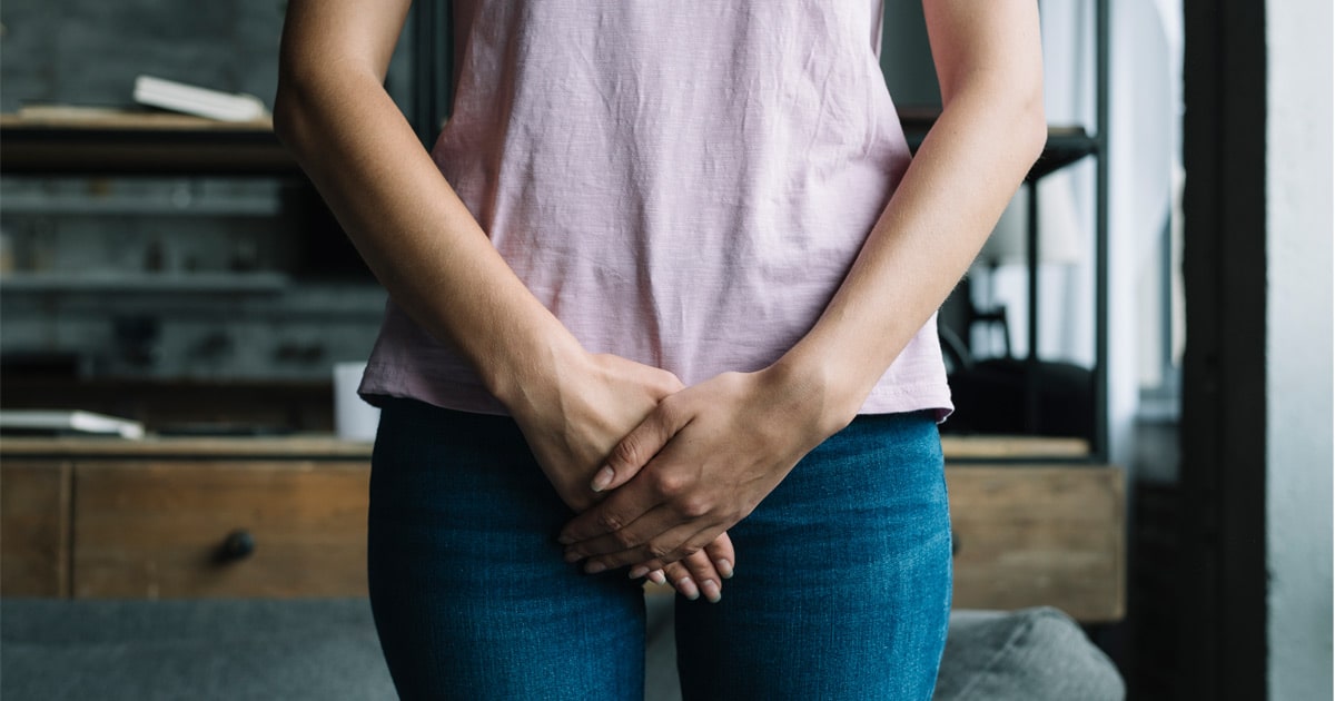 Femme qui a les deux mains croisées devant son entrejambe