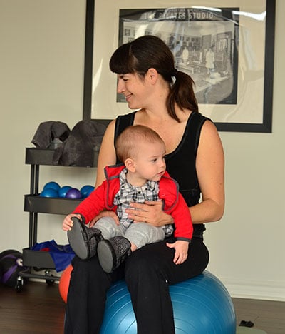 smiling mom sitting on ball with baby in arms